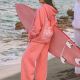 matching coral pink set, with pink palm puff pattern border. girl holding surfboard, going to the beach, aesthetic beach photo