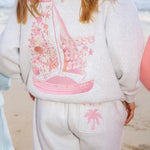 Matching heather grey sweat set with Pink Palm Puff shell pattern border. Walking toward the beach, shot from behind. Overcast soft light, cool tones, wet sand reflection, muted ocean horizon. Aesthetic beach editorial, film grain.