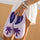 Person holding a pair of purple Malibu slippers by Pink Palm Puff with palm tree design on a blurred background